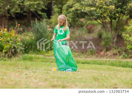 School-age girl holding green trash bag and picking up plastic bottles and litter at park School-age girl holding green trash bag and picking up plastic bottles and litter at park 132983754