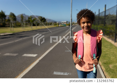 African American girl holding pink backpack on sidewalk beside road pavement markings, copy space African American girl holding pink backpack on sidewalk beside road pavement markings, copy space 132983762