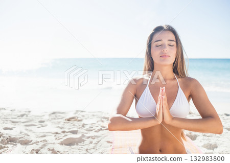 Woman in white bikini top meditating on striped yoga mat on beach with waves, copy space 132983800