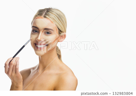 Female model in strapless top applying contour makeup with brush on cheek in studio, copy space 132983804