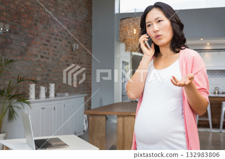 Pregnant Asian woman standing in home interior calling on smartphone by laptop on table, copy space Pregnant Asian woman standing in home interior calling on smartphone by laptop on table, copy space 132983806