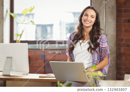 Woman in cardigan holding laptop while sitting at desk with plants in office space, copy space Woman in cardigan holding laptop while sitting at desk with plants in office space, copy space 132983807