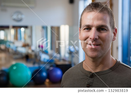 Male trainer standing in pilates gym with equipment, mirrored wall and window frames, copy space Male trainer standing in pilates gym with equipment, mirrored wall and window frames, copy space 132983819