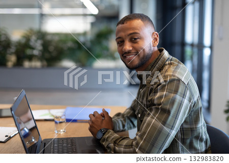 Mid adult African American man using laptop in office with binder, clipboard and water Mid adult African American man using laptop in office with binder, clipboard and water 132983820
