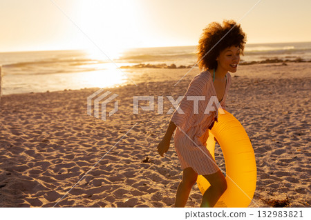 African American woman walking along shoreline at sunset holding yellow inflatable ring, copy space African American woman walking along shoreline at sunset holding yellow inflatable ring, copy space 132983821