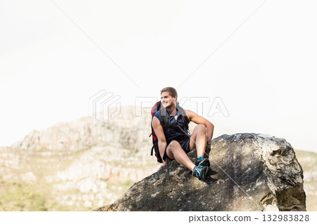 Male hiker sitting on boulder on rocky hillside wearing hiking backpack and trail shoes and smiling Male hiker sitting on boulder on rocky hillside wearing hiking backpack and trail shoes and smiling 132983828