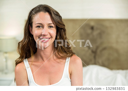 Woman wearing white top sitting on edge of bed in bedroom with headboard and nightstand lamp 132983831