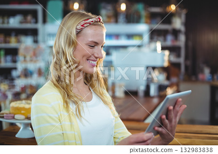 Woman standing at wooden counter in coffee shop holding tablet beside white cake stand 132983838