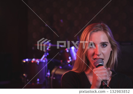 Female singer singing into microphone on stage under purple lights with drum kit, copy space 132983852