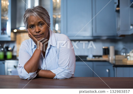 Senior African American woman leaning on wood countertop in kitchen observing shaker-style cabinets 132983857
