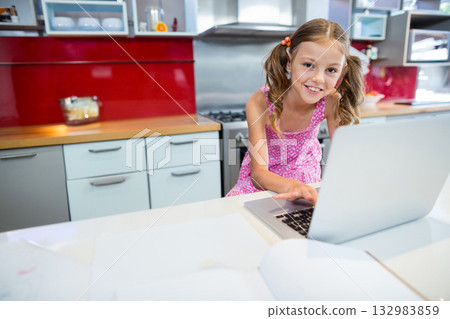 Female child smiling and leaning toward open laptop on white countertop in home kitchen, copy space Female child smiling and leaning toward open laptop on white countertop in home kitchen, copy space 132983859
