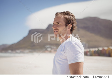 Man wearing white T-shirt standing gazing toward horizon on sandy shore with beach huts, copy space Man wearing white T-shirt standing gazing toward horizon on sandy shore with beach huts, copy space 132983861