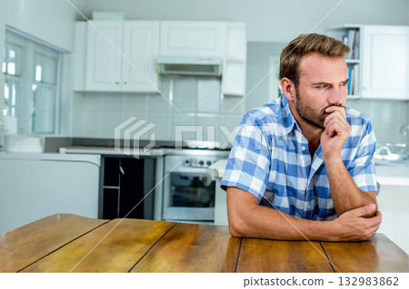 Middle-aged man leaning on wooden table in modern kitchen with stainless steel stove, copy space 132983862
