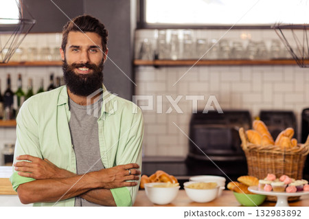 Male baker standing behind counter in bakery showing croissants, baguettes and cupcakes, copy space 132983892