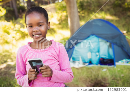 African American girl exploring forest holding smartphone near blue camping tent, copy space African American girl exploring forest holding smartphone near blue camping tent, copy space 132983901