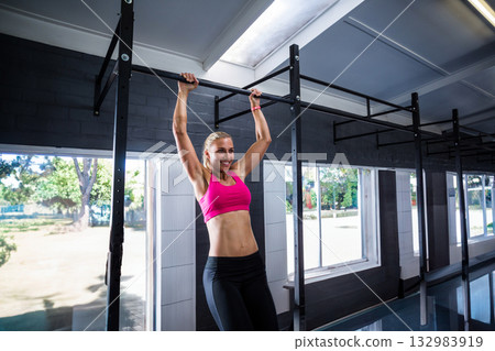 Woman in pink sports bra and black leggings performing pull-up on horizontal bar in gym Woman in pink sports bra and black leggings performing pull-up on horizontal bar in gym 132983919