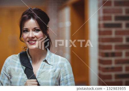 Woman standing in blurred corridor holding shoulder bag strap and wearing stud earrings, copy space 132983935