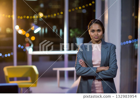 Asian woman standing arms crossed wearing blazer in office lounge under string lights, copy space 132983954