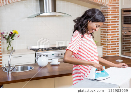 African American woman ironing garment on ironing board in kitchen with steam iron, copy space 132983969