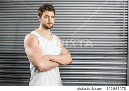 Muscular man posing with arms crossed in garage beside corrugated roller shutter door, copy space Muscular man posing with arms crossed in garage beside corrugated roller shutter door, copy space 132983978