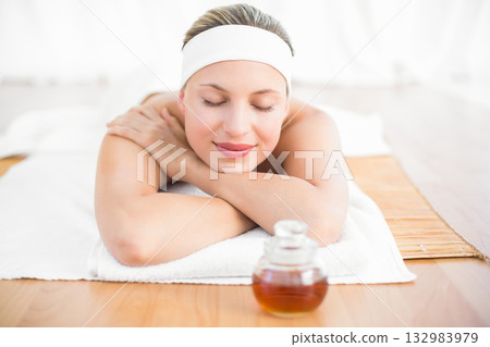 Woman lying face down on towel at spa wearing headband beside massage oil jar, bamboo mat Woman lying face down on towel at spa wearing headband beside massage oil jar, bamboo mat 132983979