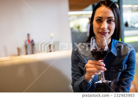 Woman sitting at bar counter holding wine glass with red wine under warm lighting, copy space 132983983