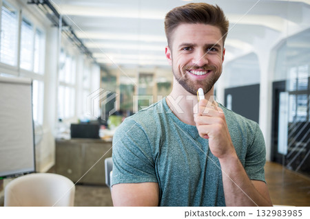 Man wearing green tee holding marker near chin beside flipchart in open-plan office, copy space 132983985