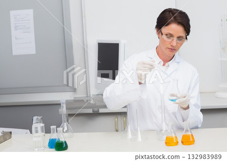 Female scientist pouring blue solution from flask into funnel with pipette at lab bench, copy space 132983989