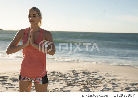 Woman standing on sandy beach at water's edge wearing coral tank top, patterned shorts, copy space Woman standing on sandy beach at water's edge wearing coral tank top, patterned shorts, copy space 132983997