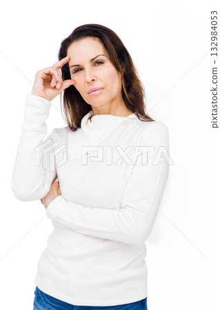 Senior woman standing in studio touching temple and wearing white knit sweater with blue jeans Senior woman standing in studio touching temple and wearing white knit sweater with blue jeans 132984053