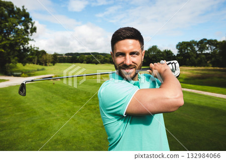 Male golfer wearing turquoise polo and golf glove holding iron club across shoulders on fairway Male golfer wearing turquoise polo and golf glove holding iron club across shoulders on fairway 132984066