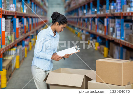 Woman holding clipboard and pen inspecting open cardboard box on pallet in warehouse aisle Woman holding clipboard and pen inspecting open cardboard box on pallet in warehouse aisle 132984070