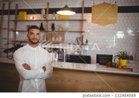 Male barista wearing white shirt operating espresso maker at cafe counter with pastries, copy space 132984089