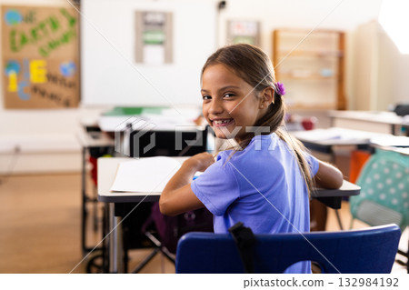 Girl child sitting at school desk turning around smiling, looking at camera with notebook, pencil 132984192
