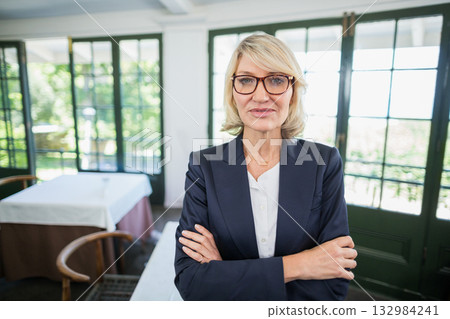 Senior woman standing wearing navy blazer and glasses at dining room tables overlooking garden Senior woman standing wearing navy blazer and glasses at dining room tables overlooking garden 132984241