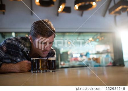 Man leaning over bar counter in brewery taproom inspecting beer flight under warm lights 132984246