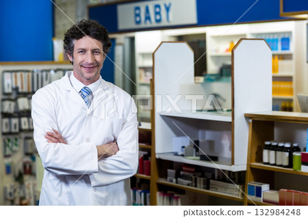 Mature pharmacist in lab coat standing at pharmacy counter with shelves under BABY sign, copy space 132984248