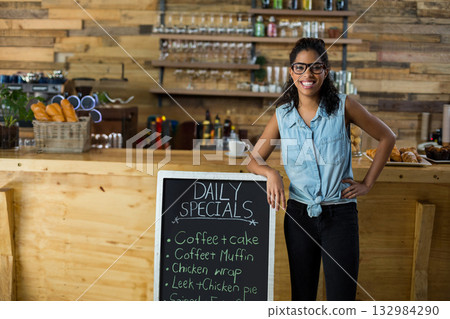 Smiling African American woman leaning behind coffee shop counter with chalkboard sign and baskets 132984290