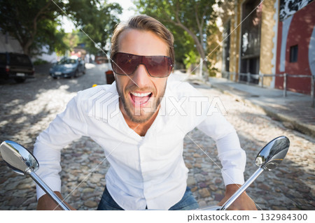Man leaning and grinning on scooter handlebars on cobblestone street with tinted sunglasses Man leaning and grinning on scooter handlebars on cobblestone street with tinted sunglasses 132984300