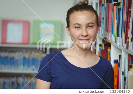 Female teenager leaning against bookshelf in library aisle browsing colorful books and artwork Female teenager leaning against bookshelf in library aisle browsing colorful books and artwork 132984320