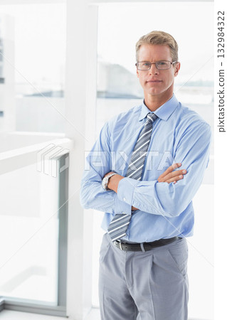 Mature adult man standing by floor-to-ceiling window in office wearing eyeglasses, tie, copy space Mature adult man standing by floor-to-ceiling window in office wearing eyeglasses, tie, copy space 132984322