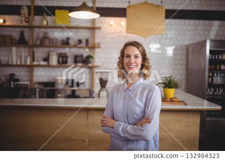 Woman in her twenties standing at wood counter in coffee shop with coffee grinder and pastries Woman in her twenties standing at wood counter in coffee shop with coffee grinder and pastries 132984323