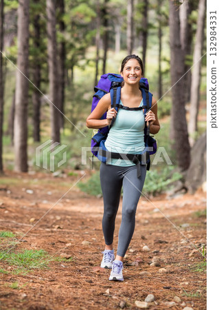 Female hiker in late twenties walking along conifer trail wearing sportswear and carrying backpack Female hiker in late twenties walking along conifer trail wearing sportswear and carrying backpack 132984331