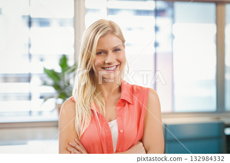 Woman standing with arms crossed wearing coral blouse smiling in office with potted plant windows Woman standing with arms crossed wearing coral blouse smiling in office with potted plant windows 132984332