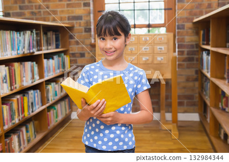 Asian girl standing in library aisle reading yellow book near card catalog by window Asian girl standing in library aisle reading yellow book near card catalog by window 132984344