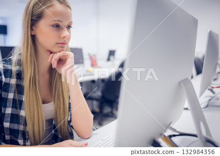 Teenage girl typing on all-in-one desktop computer at lab desk with rows of monitors, copy space 132984356
