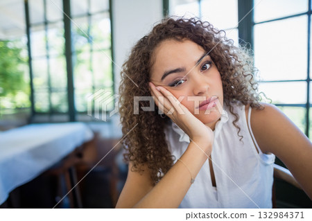 Woman leaning on hand wearing bracelet, gazing ahead at wooden table by grid windows, copy space Woman leaning on hand wearing bracelet, gazing ahead at wooden table by grid windows, copy space 132984371