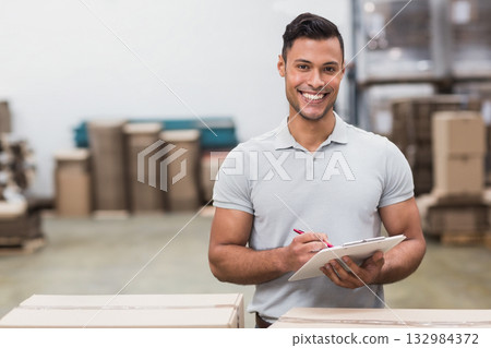 Male warehouse worker checking inventory with clipboard and pen in large warehouse, copy space Male warehouse worker checking inventory with clipboard and pen in large warehouse, copy space 132984372