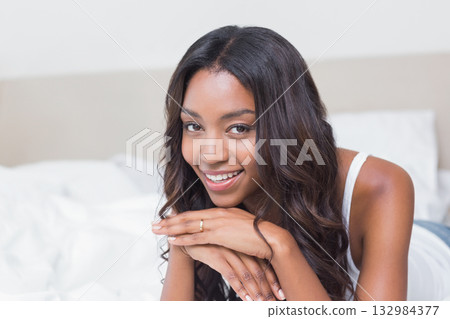 African American woman lying on bed wearing white tank top resting on hands showing gold ring 132984377