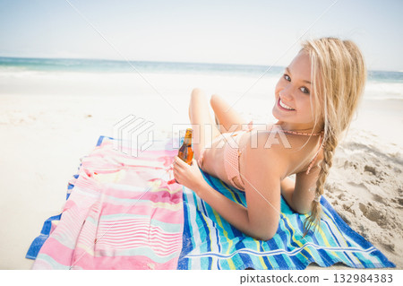Woman lying on striped towel at sandy shore in pink bikini holding brown bottle, copy space Woman lying on striped towel at sandy shore in pink bikini holding brown bottle, copy space 132984383